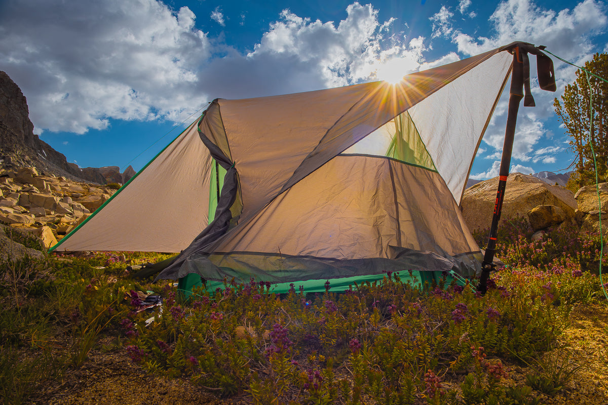 Tent set up in a mountainous area with a sunlit sky