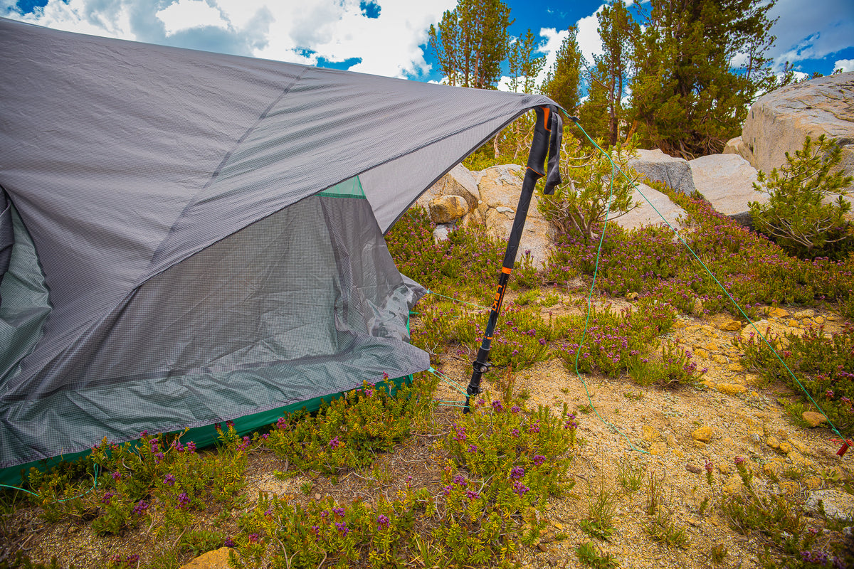 Gray camping tent set up in a natural outdoor setting with trees and rocks.
