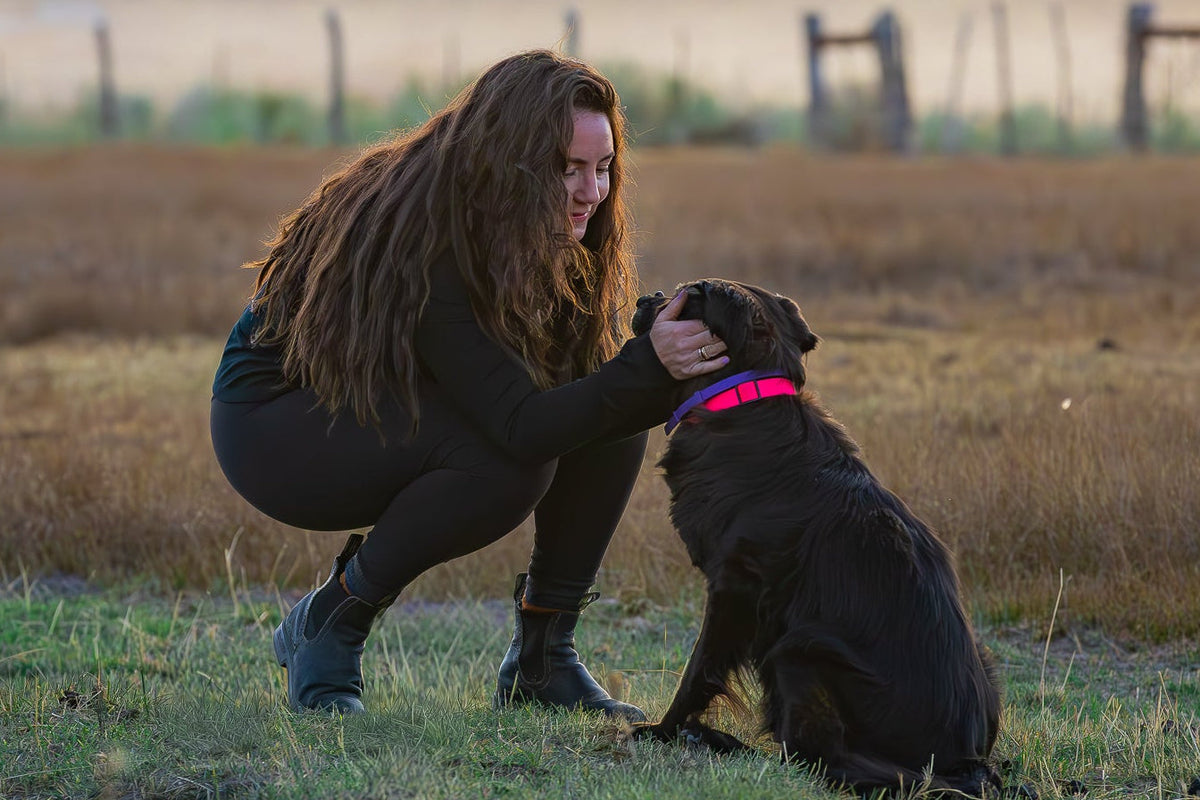 Woman kneeling down with a dog in a field with mountains in the background