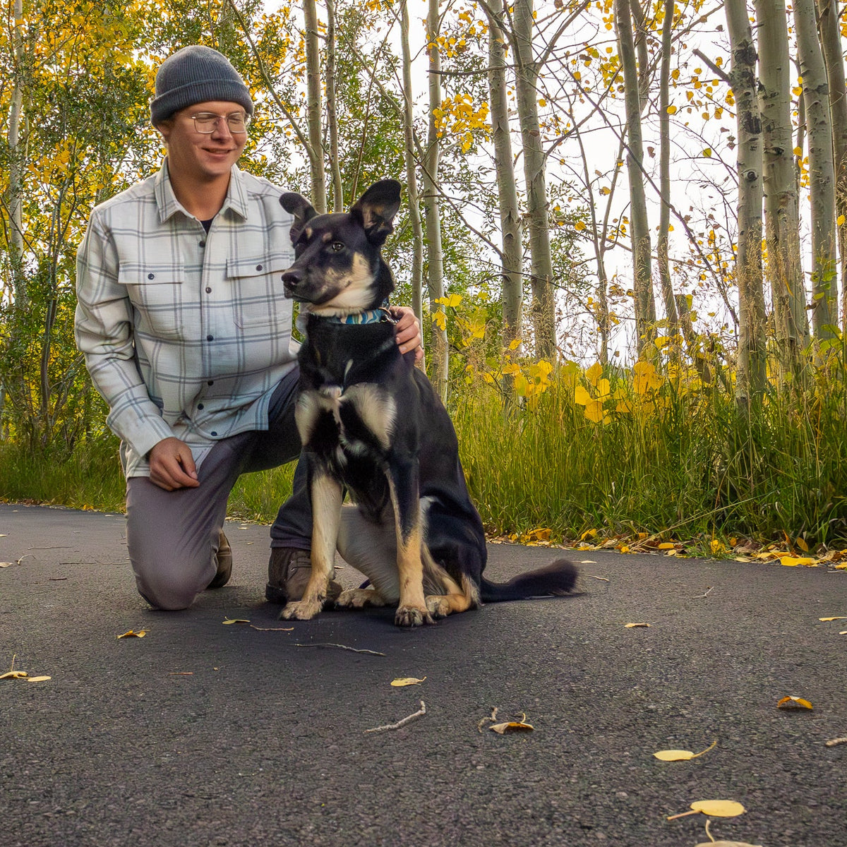 Man kneeling on a path with a dog, surrounded by trees and grass