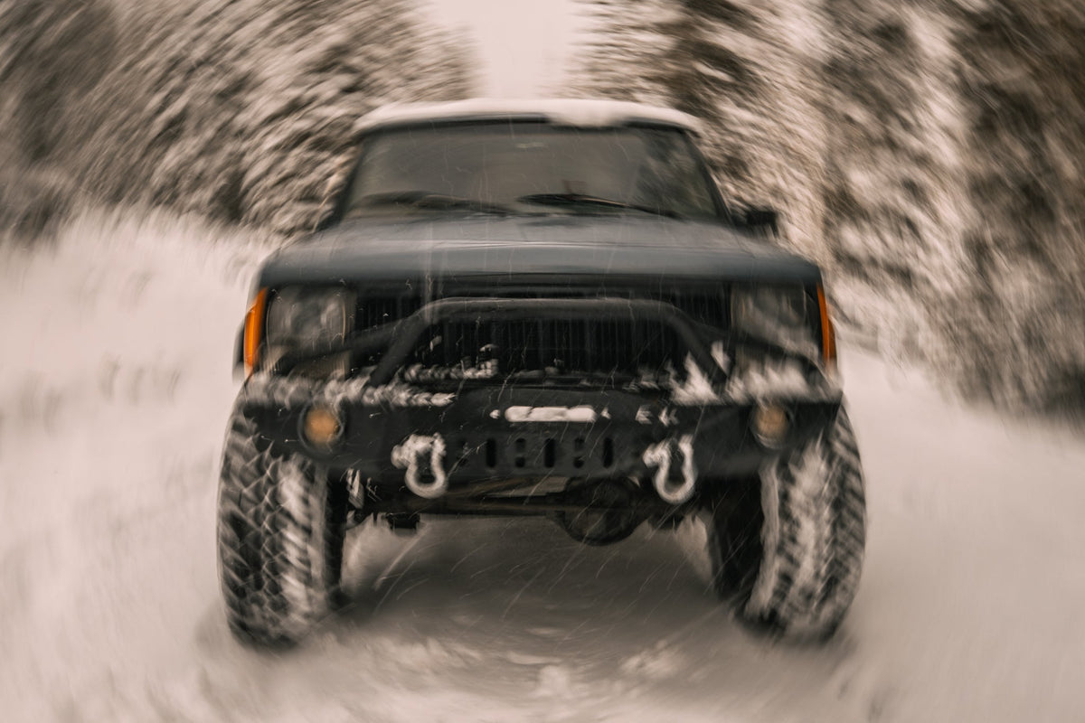 Black off-road vehicle driving on a snowy path with blurred trees in the background